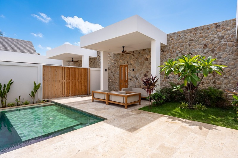 Stone-walled sala with carved teak door and lounge seating at the end of the pool